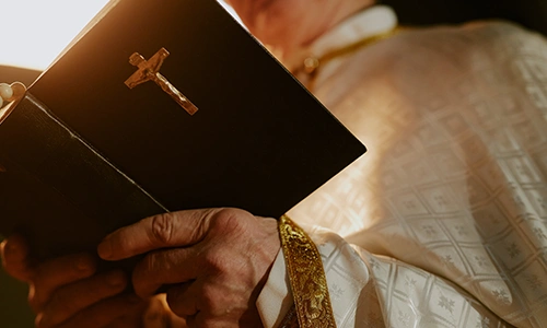 papst Symbolbild: Ein Geistlicher im liturgischen Gewand hält eine geschlossene Bibel mit goldenem Kruzifix in den Händen
